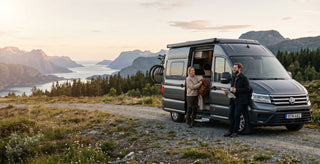 A woman and a man standing in front of a campervan in the middle of the nature